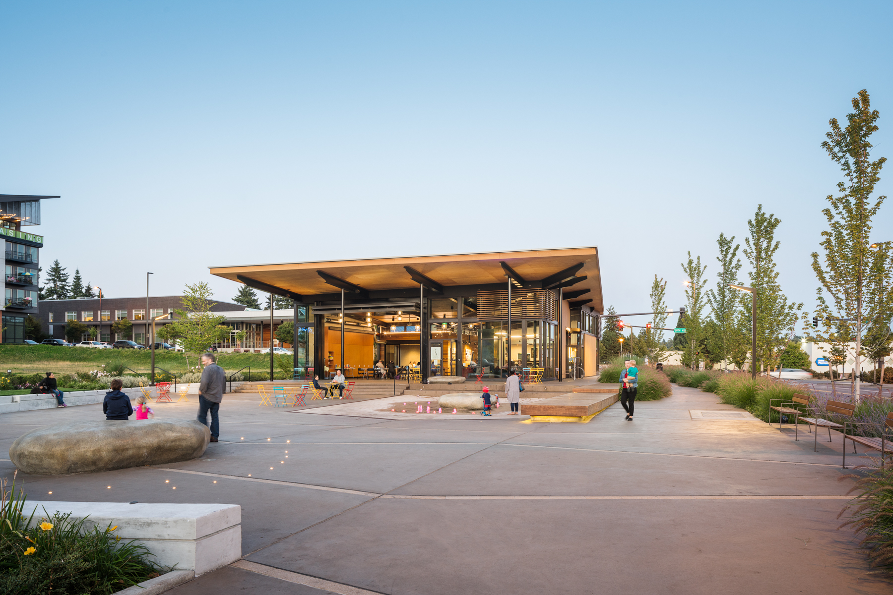 The Hangar at Town Square with people recreating at tables and the splash pad on a Summer day.