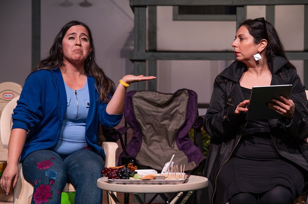 Two women on stage performing "Cry It Out" next to a charcuterie board.