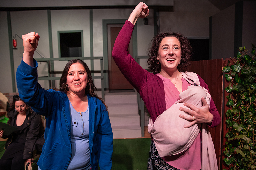 Two performers smiling and triumphantly raising their fists on stage.