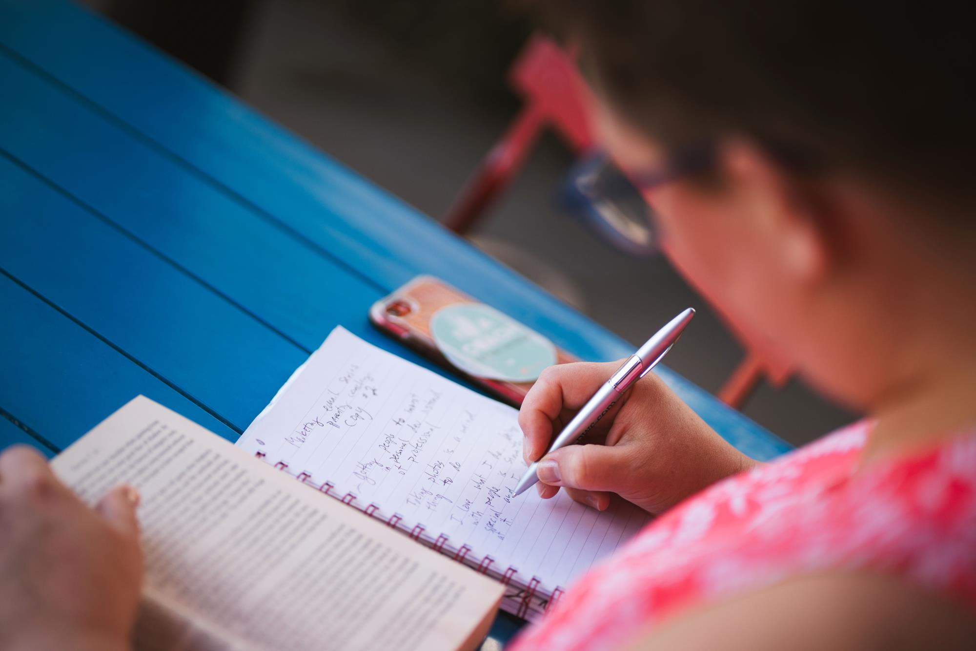 A student writes notes in their journal as they read a book. 